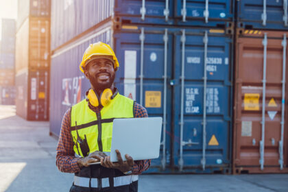 Black African staff workerworking in cargo shipping logistic port with laptop computer.